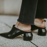 Women in black, formal pants, wearing a pair of black mules shoes for women.